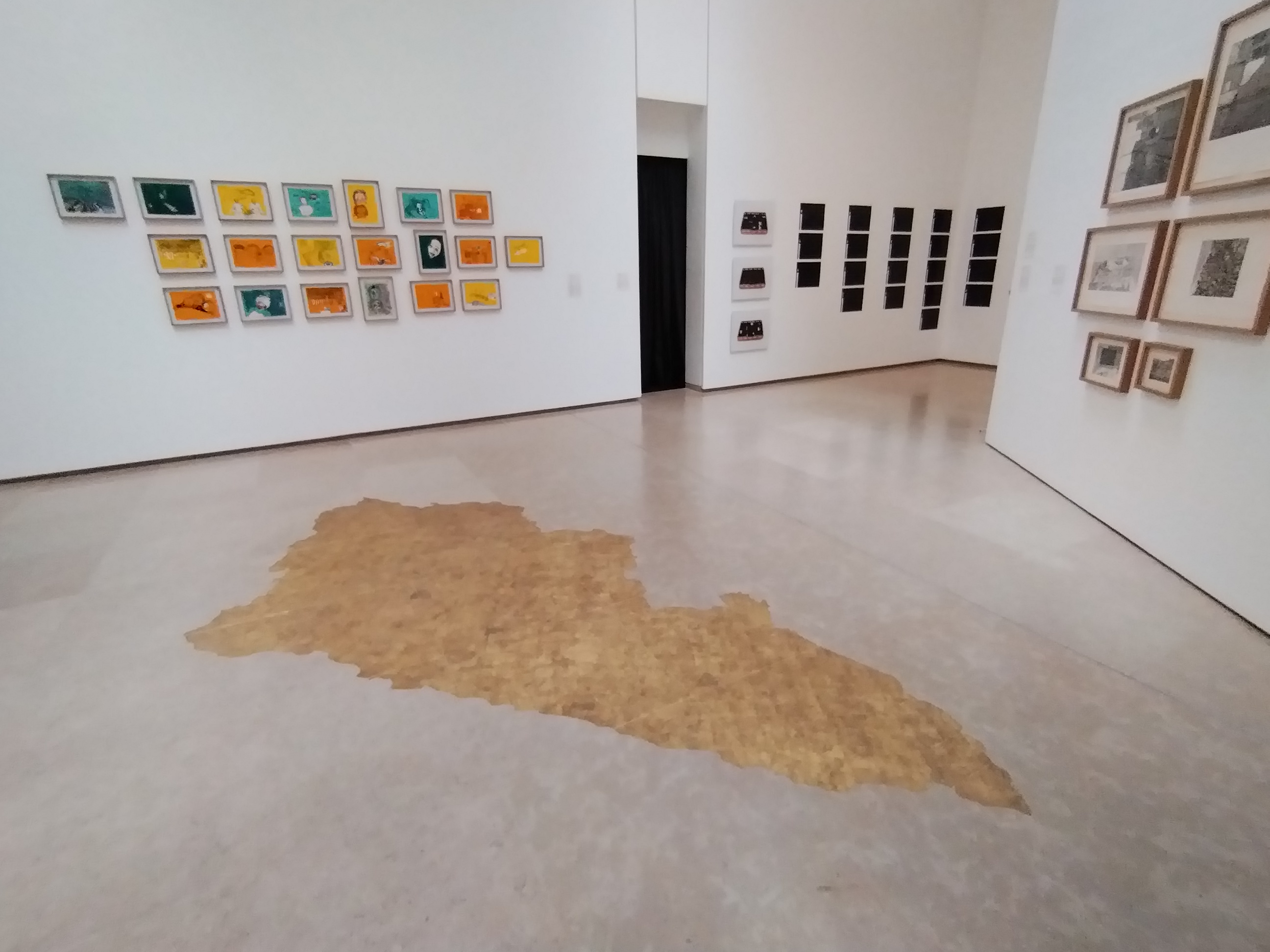 view of gallery interior with a spill of gold paint on the floor in the foreground